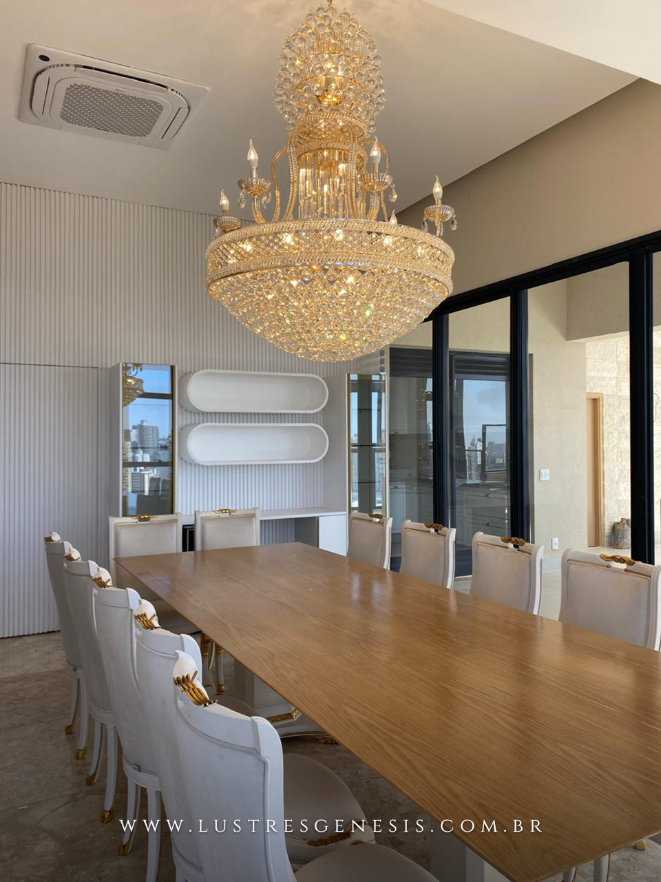 Lustre de cristal clássico dourado com cristais transparentes instalado acima de uma mesa de jantar grande em sala sofisticada.